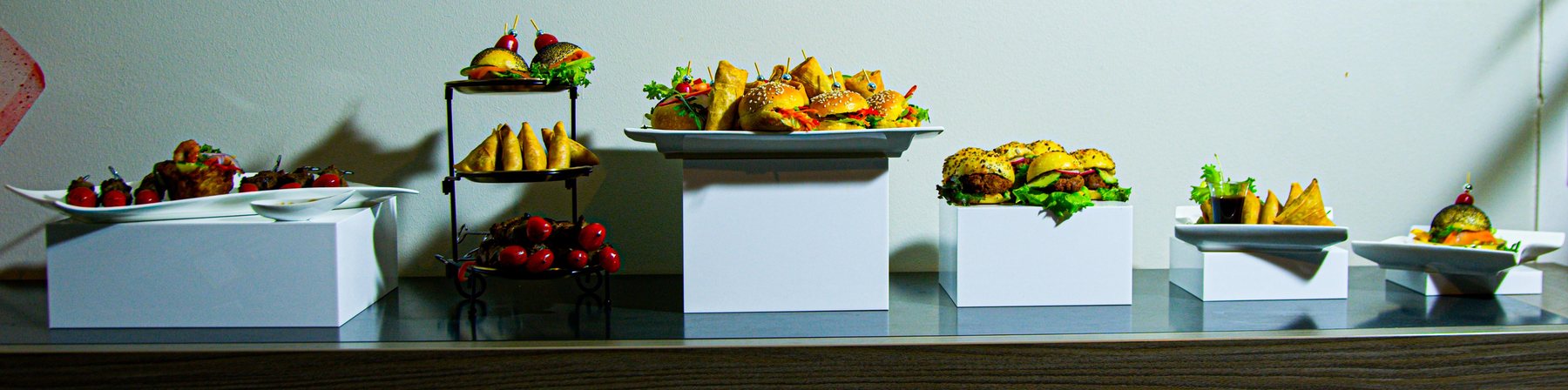 Buffet traiteur dressé sur présentoirs : mini-burgers, samoussas et brochettes marinées