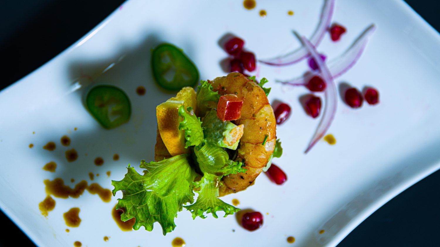 Crevette rôtie dressée à l'assiette, éclats de grenade, jalapeño et oignon rouge