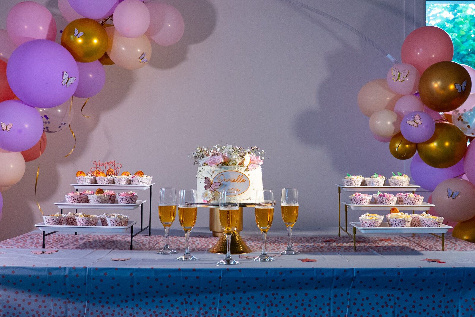 Table de fête dressée, gâteau central, cupcakes et arche de ballons